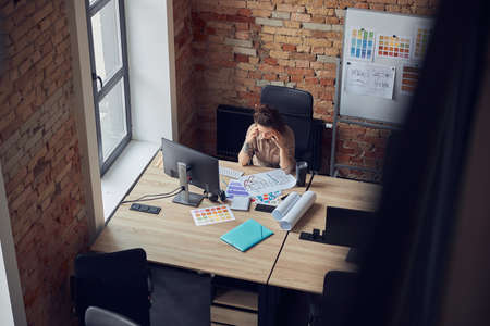 High angle view of tired woman touching her temples, having a stong headache while working on new project, using pc in modern officeの写真素材