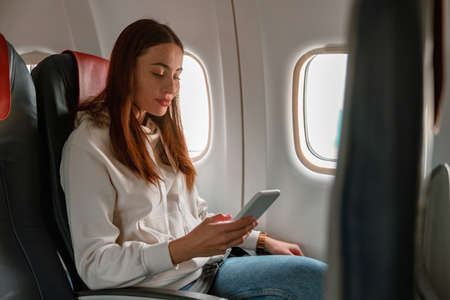 Female passenger using mobile phone in airplaneの写真素材