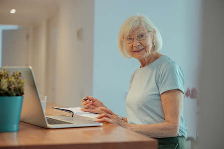 Portrait of joyful senior woman with laptop indoorsの写真素材