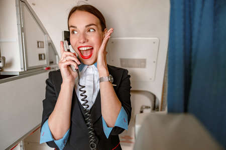 Cheerful flight attendant talking on telephone in airplaneの写真素材