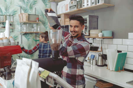 smiling man barista pouring beans into the coffee grinderの写真素材