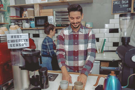 Young smiling barista with mustache serving customersの写真素材