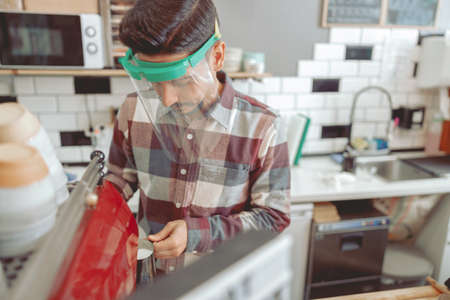 Portrait of man barista working at cafe in protective visorの写真素材