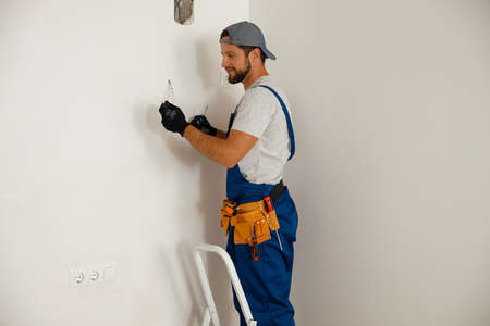 Busy handyman electrician holding screwdriver while working on residential electric systemの写真素材