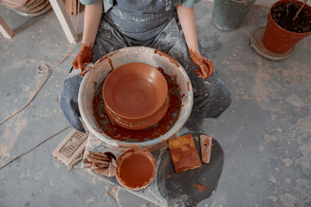 Skillful female potter creating earthen bowl on circle in workroomの写真素材