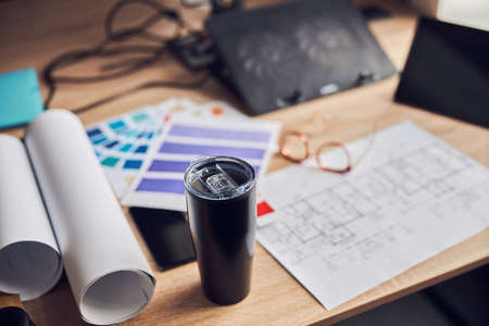 Close up shot of flask on creative desk. Architectural blueprint with color samples, tablet pc and glassesの写真素材