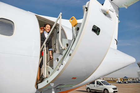 Joyful woman flight attendant closing airplane doorの写真素材