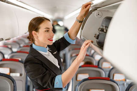 Joyful stewardess checking overhead luggage bin in airplaneの写真素材