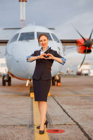 Cheerful flight attendant showing heart sign at airportの写真素材