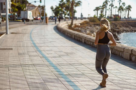Sporty young woman jogging on sidewalk in public parkの写真素材