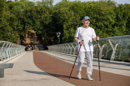 Senior sportsman practices Nordic walking training on empty footbridgeの写真素材