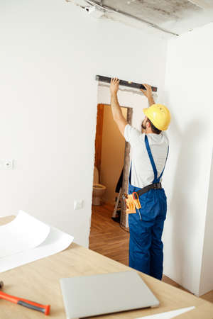 Busy handyman, male worker in uniform checking the wall with spirit levelの写真素材