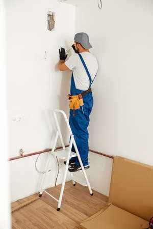 Electrician, handyman standing on a ladder while working on installing socket on wall at homeの写真素材