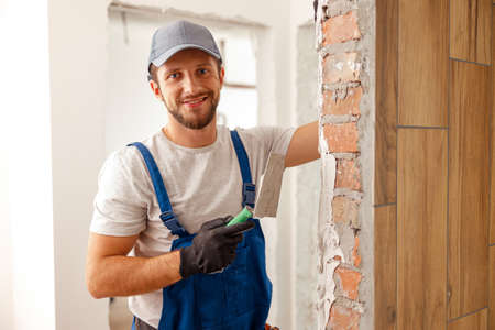 Portrait of hard working handyman or craftsman smiling at camera while filling the wall, preparing...