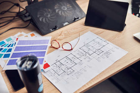 Close up shot of interior designer workplace. Glasses, architectural blueprint with color samples, tablet pc and smartphone on creative deskの写真素材