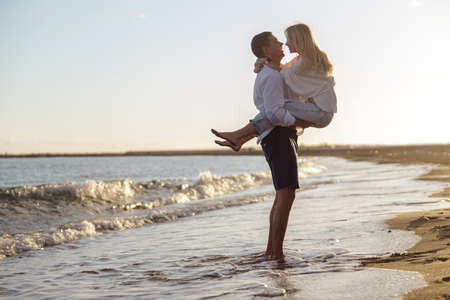 Full length photo of man holding woman in his arms standing by the seaの写真素材