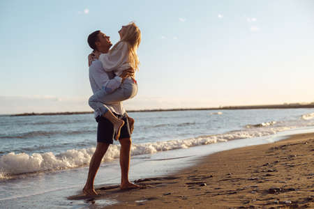 Carefree couple having fun standing on seashore at sunsetの写真素材