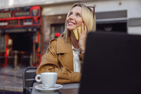 Portrait of smiling woman sitting at table in street cafe calling on phoneの写真素材