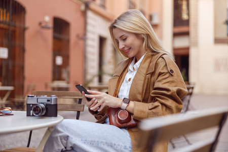 Side photo of happy female holding smartphone and sitting at tableの写真素材