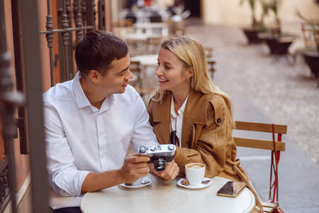 Smiling woman sitting at table of street cafe with handsome man and reviewing photosの写真素材