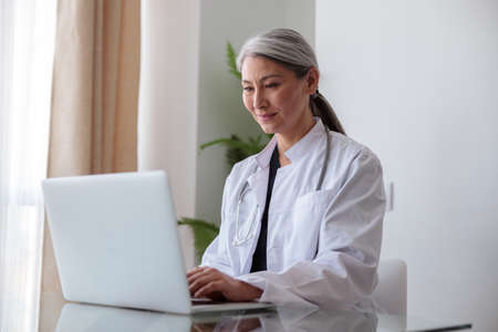 Focused woman medical specialist typing on laptop sitting at officeの写真素材