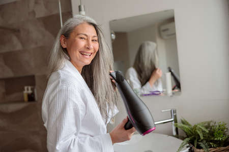 Smiling lady styling hair after taking a bathの写真素材