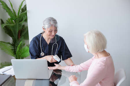 Doctor in protective visor examining patient at homeの写真素材