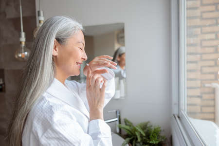 Portrait of smiling lady in the bathroom sniffing creamの写真素材