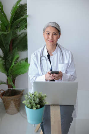 Smiling doctor sitting at office with laptop on deskの写真素材