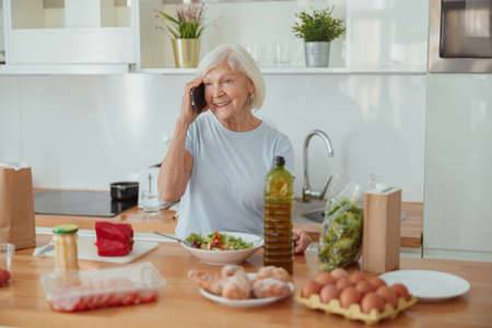 Happy aged female talking on mobile phone indoorsの写真素材