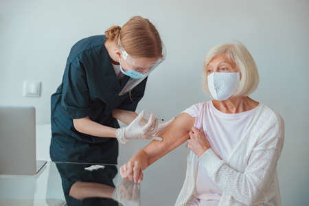 Nurse giving injection to senior woman in living roomの写真素材
