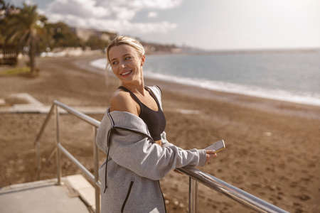 Smiling sporty woman using smartphone on beachの写真素材