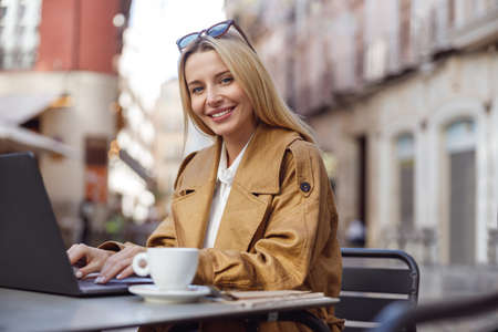 Portrait of woman dressed in trench coat working with laptop outsideの写真素材