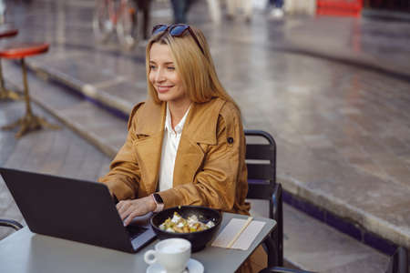 Young lady dressed in trench coat sitting at table in street cafeの写真素材