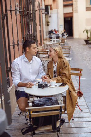 Lovely couple sitting at table on street near cafe and talkingの写真素材