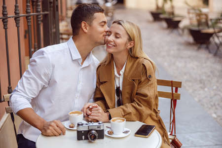 Loving man kissing his girlfriend on cheek during date in street cafeの写真素材