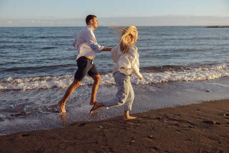 Side photo of couple running along the beach holding handsの写真素材