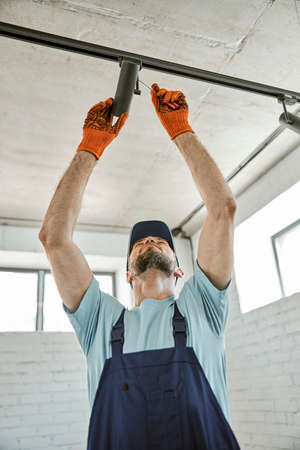 Bearded young man fixing ceiling lamp in buildingの写真素材
