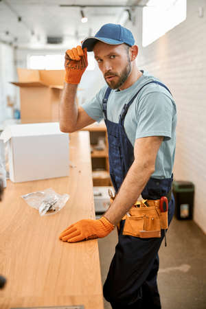 Bearded repairman in cap standing by the tableの写真素材