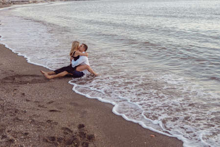 Full-length photp of man sitting on sand and woman sitting on his legsの写真素材