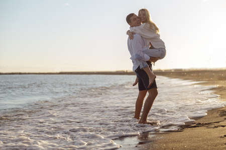 Full length of carefree couple having fun standing on seashore at sunsetの写真素材