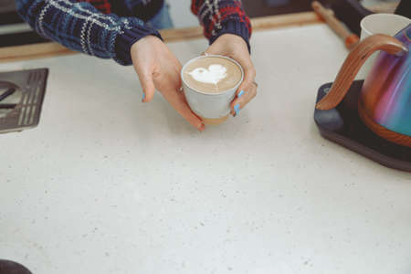 Woman holding coffee with pattern on milk over bar counterの写真素材