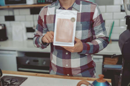 Barista wearing plaid shirt holding coffee packの写真素材