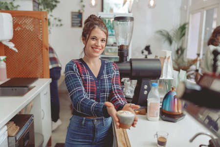 Smiling woman barista holding cup of cappuccinoの写真素材
