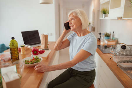 Retired woman communicating at cozy home kitchenの写真素材
