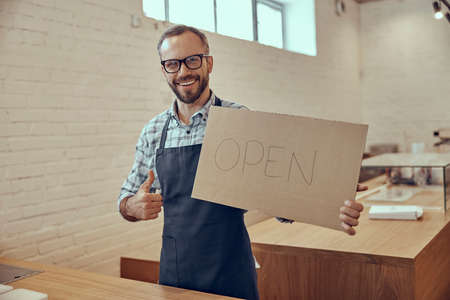 Cheerful man holding open sign and giving thumbs upの写真素材