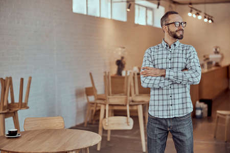 Joyful bearded man in glasses standing in cafeの写真素材