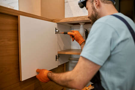 Young man in gloves fixing kitchen cupboard doorの写真素材