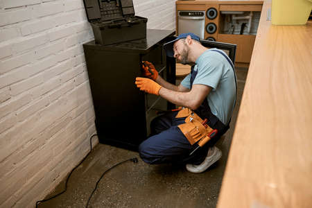 Bearded young man repairing fridge in kitchenの写真素材