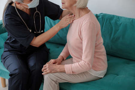 Medical worker touching a neck of an elderly womanの写真素材